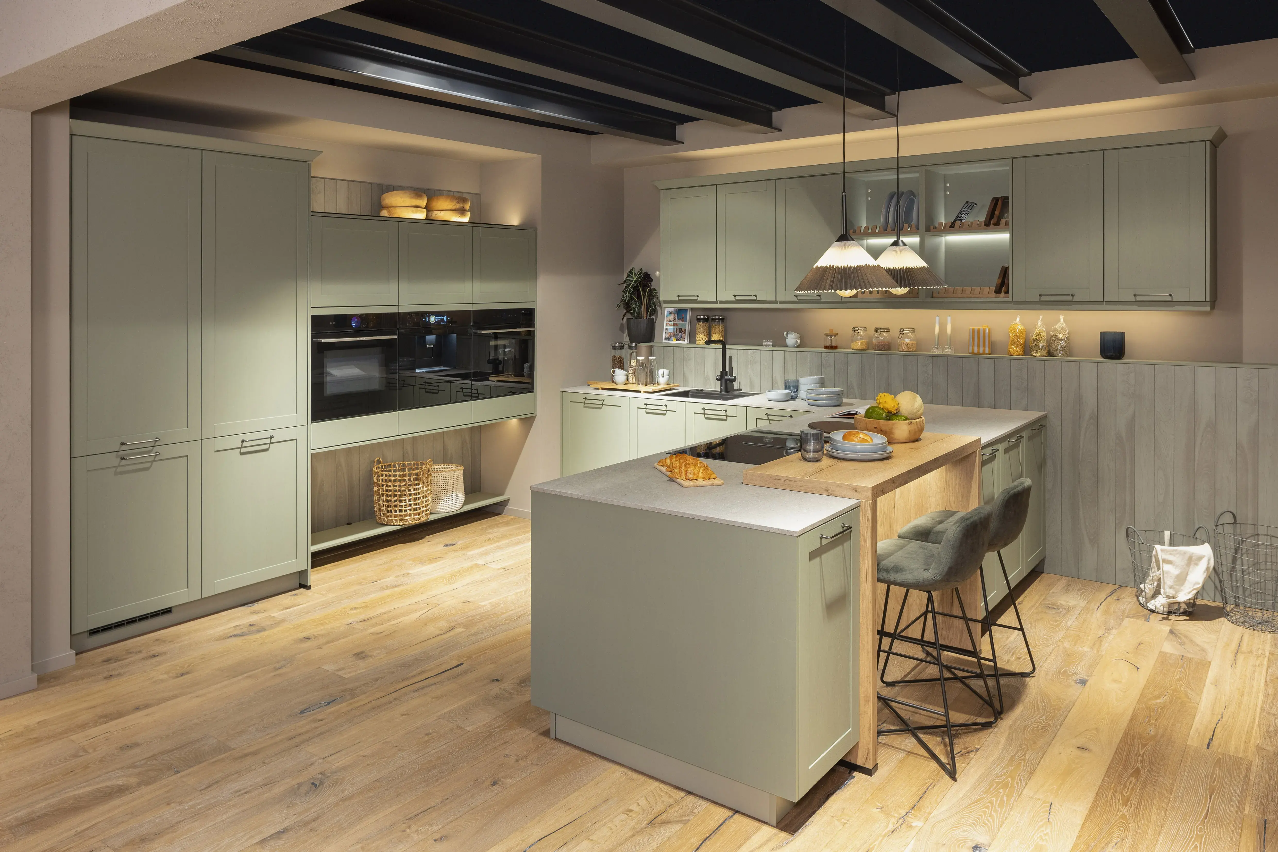 Moderne Küche mit Kochinsel, Holzfußboden und grünen Schränken, warm beleuchtet.