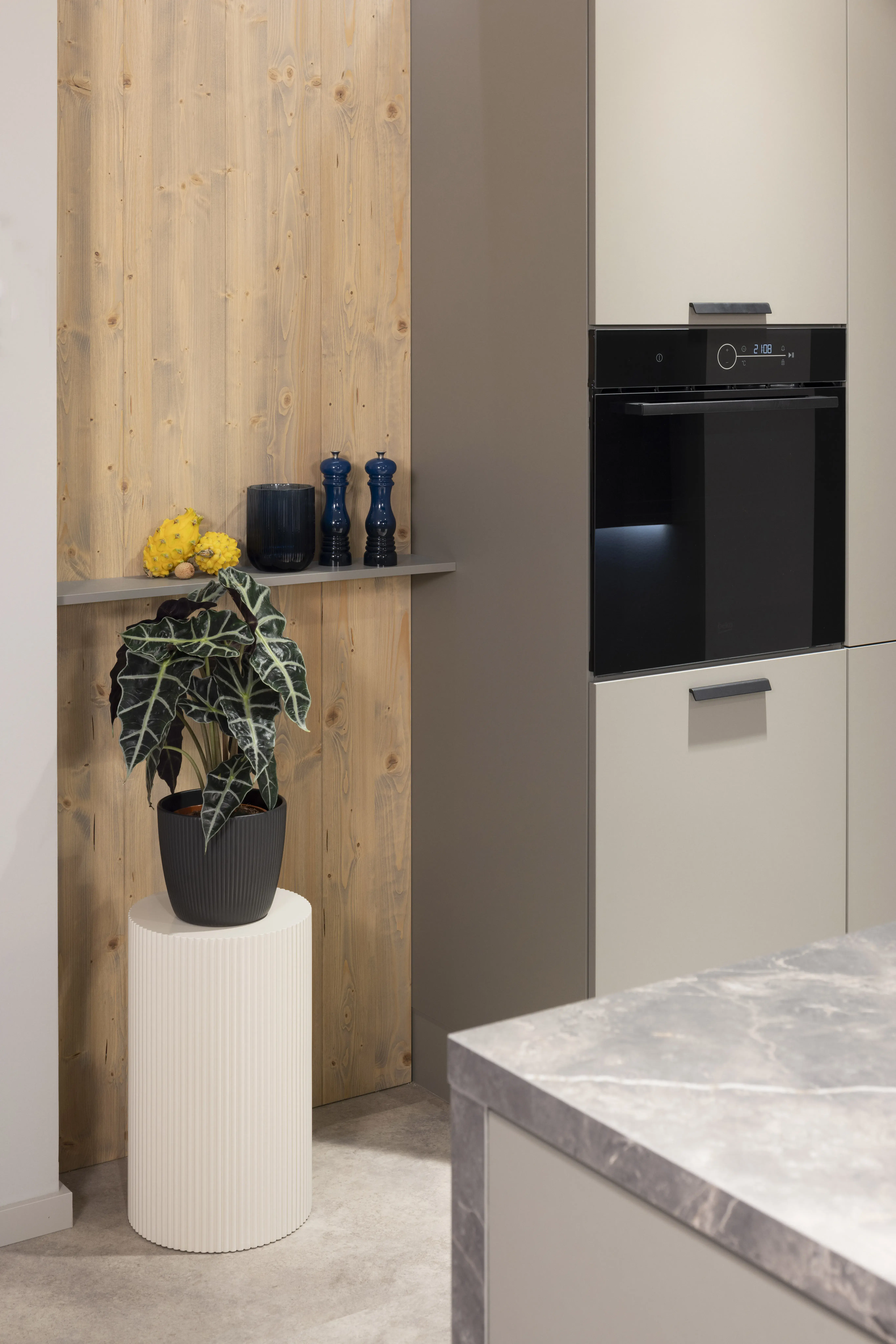 Moderne Küche mit grauem Backofen, Pflanze und Deko auf Holzregal.